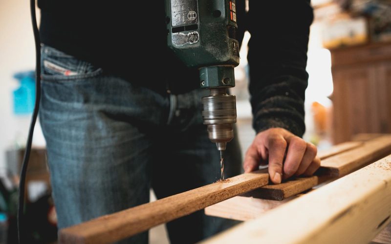 Close-up of a person using an electric drill on a wooden plank, showcasing detailed woodworking skills.