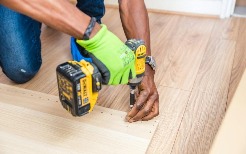 Close-up of handyman drilling wood indoors with green gloves and cordless drill.