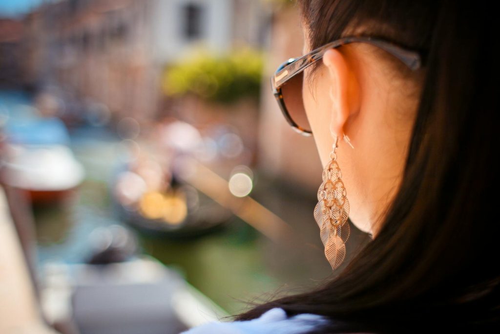 Close-up shot of a stylish woman with sunglasses and earrings overlooking a Venetian canal.
