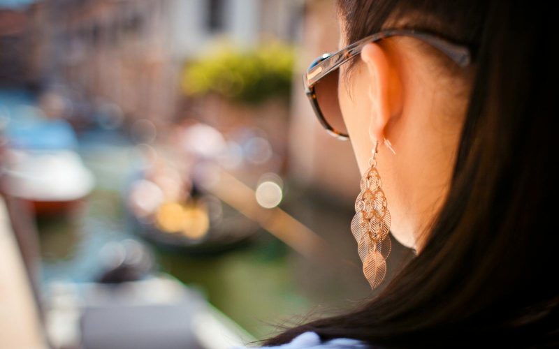 Close-up shot of a stylish woman with sunglasses and earrings overlooking a Venetian canal.