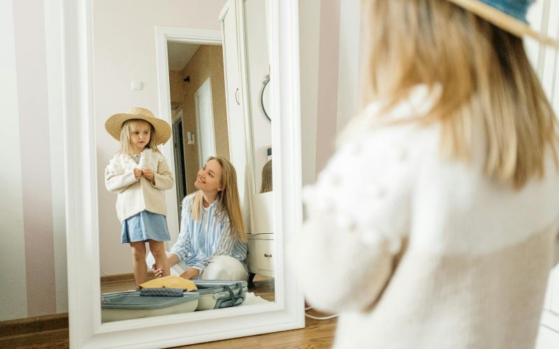 A mother and young daughter share a joyful moment dressing up indoors.